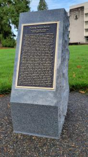 Granite and bronze monument honoring Black pioneer George Bush and his family as viewed from the front where a plaque dictates the story of the family and their significance to Washington state.