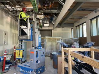 An inside look at the Irv Newhouse Building replacement project shows a worker on a genie lift working on the in-ceiling electrical.