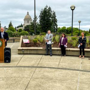 Governor Jay Inslee stands at a podium in front of the garden with the capitol building in the background