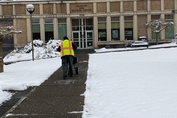 A DES employee spreads ice melt on the sidewalk in front of the State Archives Building.